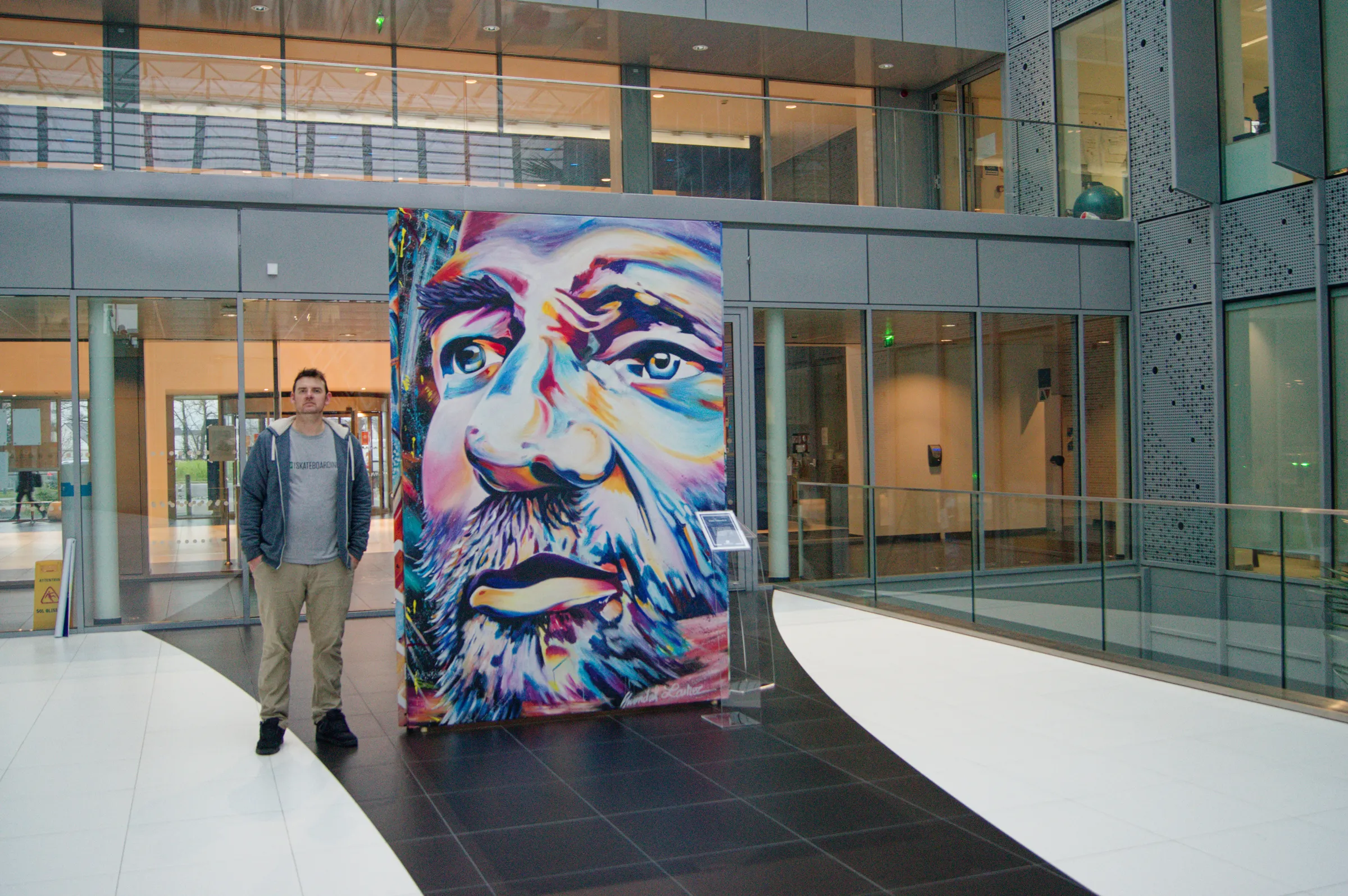 Portrait géant d'Éric Tabarly peint sur toile et exposé dans le patio du siège de la Banque Populaire Grand Ouest à Rennes, avec un visiteur pour l'échelle